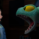 A young girl in pigtails and overall screams at an aquamarine dragon, which roars back at her.